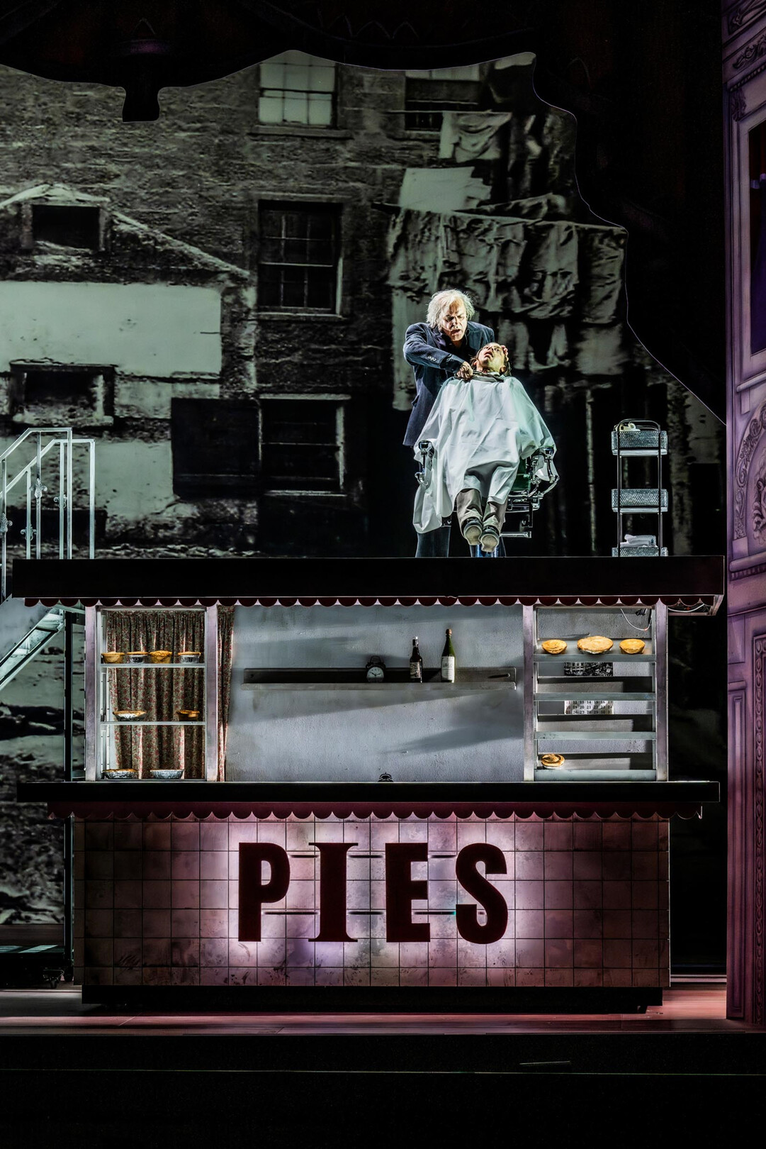 Sweeney Todd sitzt auf auf dem Dach von Mrs. Lovett Pie Shop, vor ihm ein Kunde auf dem Friseurstuhl, Sweeney Todd setzt das Messer am Hals des Kunden an